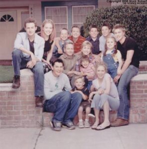 A multi-generational family posing for a group photo on the front steps of a suburban house, smiling at the camera.