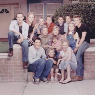 A multi-generational family posing for a group photo on the front steps of a suburban house, smiling at the camera.