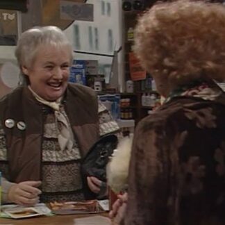 Two elderly women in a shop, a smiling cashier behind the counter greeting a customer facing away from the camera.